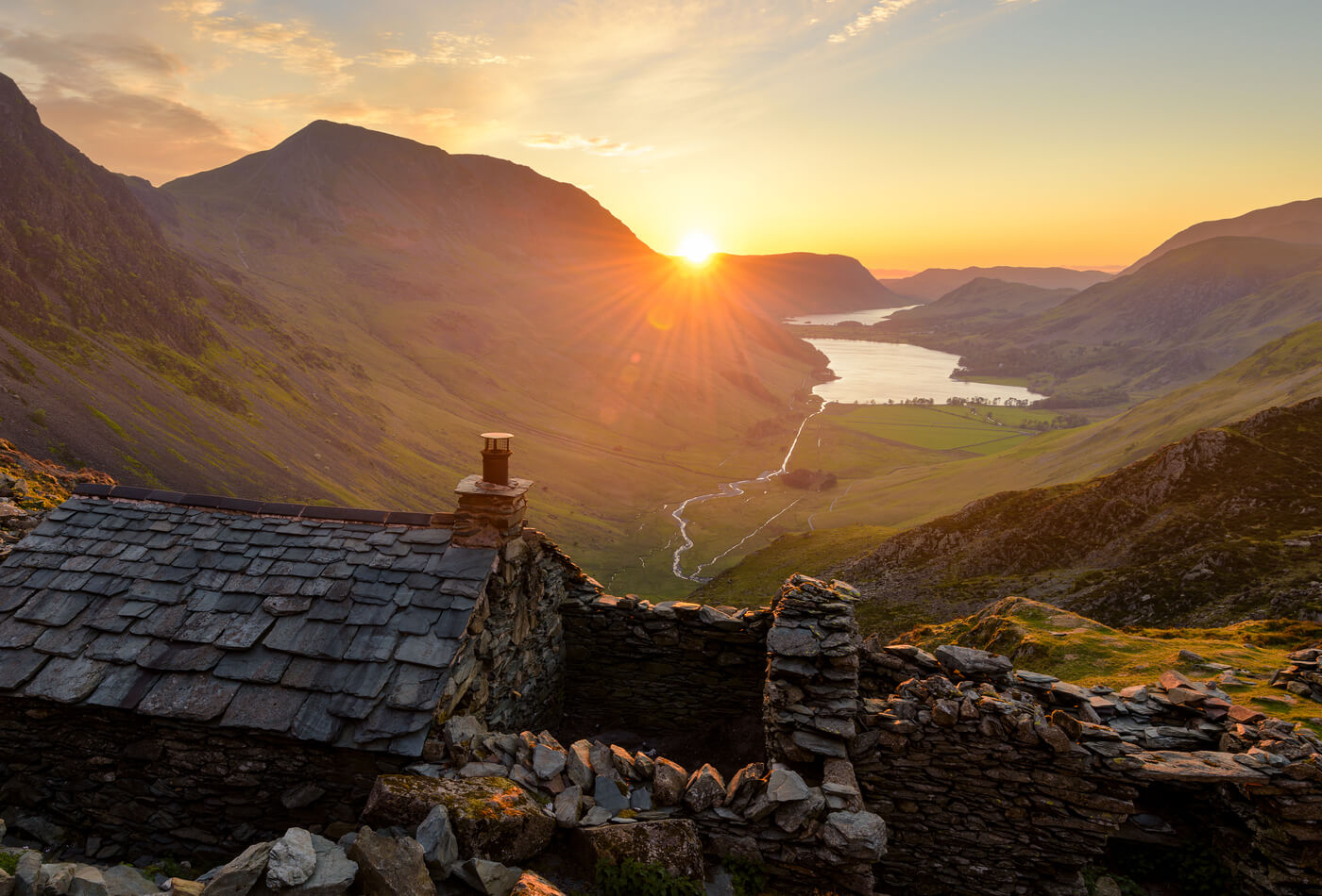 A sunset over a stonebuilt cottage with a mountanous backdrop in the Lake District